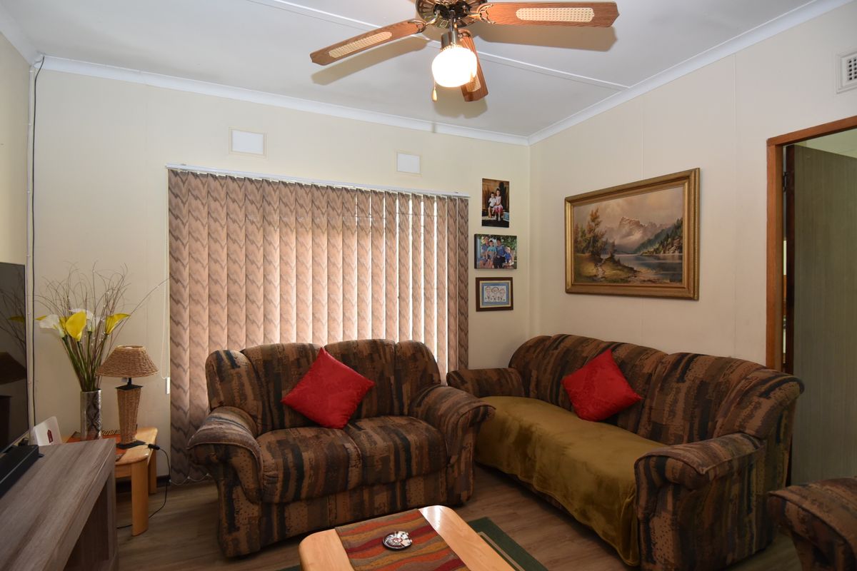 A comfortable living room featuring laminate flooring, a ceiling fan, and vertical blinds, offering a functional and well-maintained space for relaxation.
