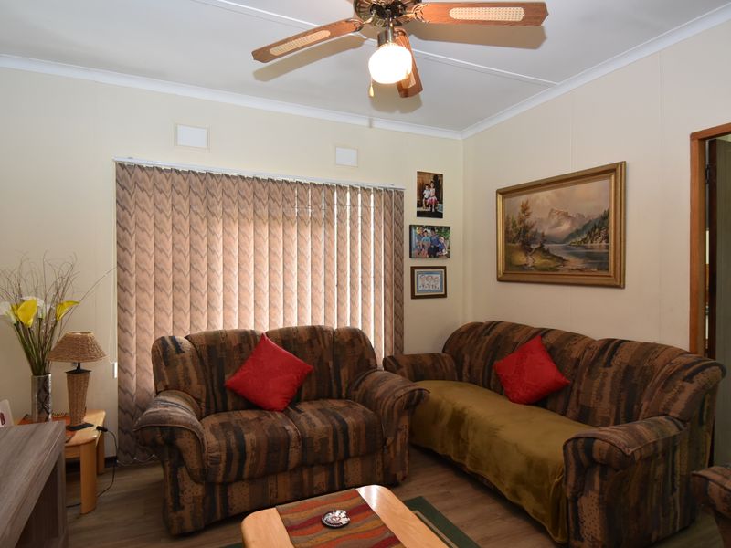 A comfortable living room featuring laminate flooring, a ceiling fan, and vertical blinds, offering a functional and well-maintained space for relaxation.
