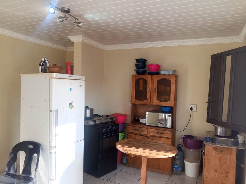 A functional kitchen area featuring wooden cabinetry, a freestanding stove, and a stainless steel sink, with tiled flooring and a tongue and groove ceiling.