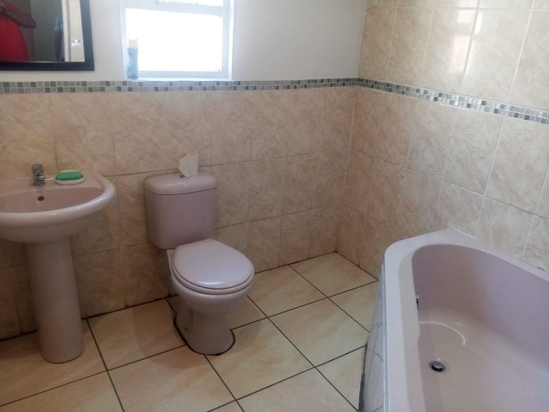 A functional bathroom featuring a pedestal basin, toilet, and bathtub with neutral wall and floor tiling.