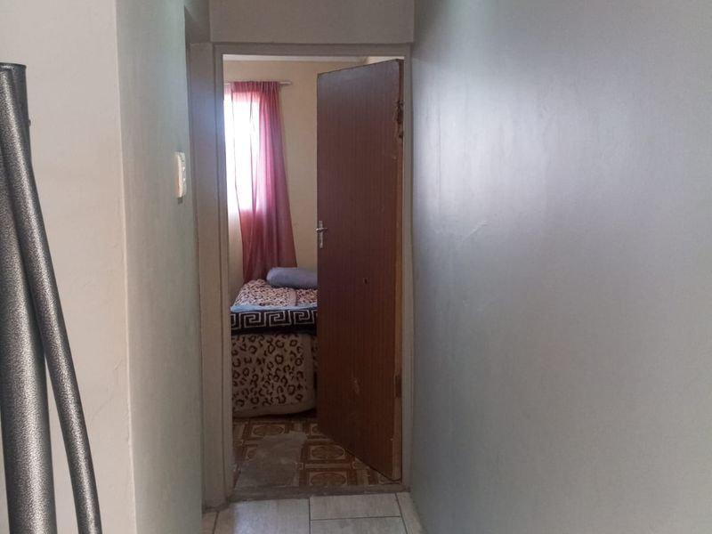 A narrow hallway featuring tiled flooring, recessed ceiling lighting, and decorative cornice, leading into a bedroom.
