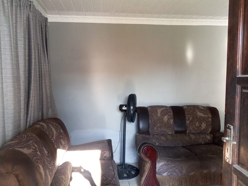 A living room area featuring tiled flooring, decorative ceiling cornice, and a timber entrance door, showing signs of wear on the lower wall surfaces.