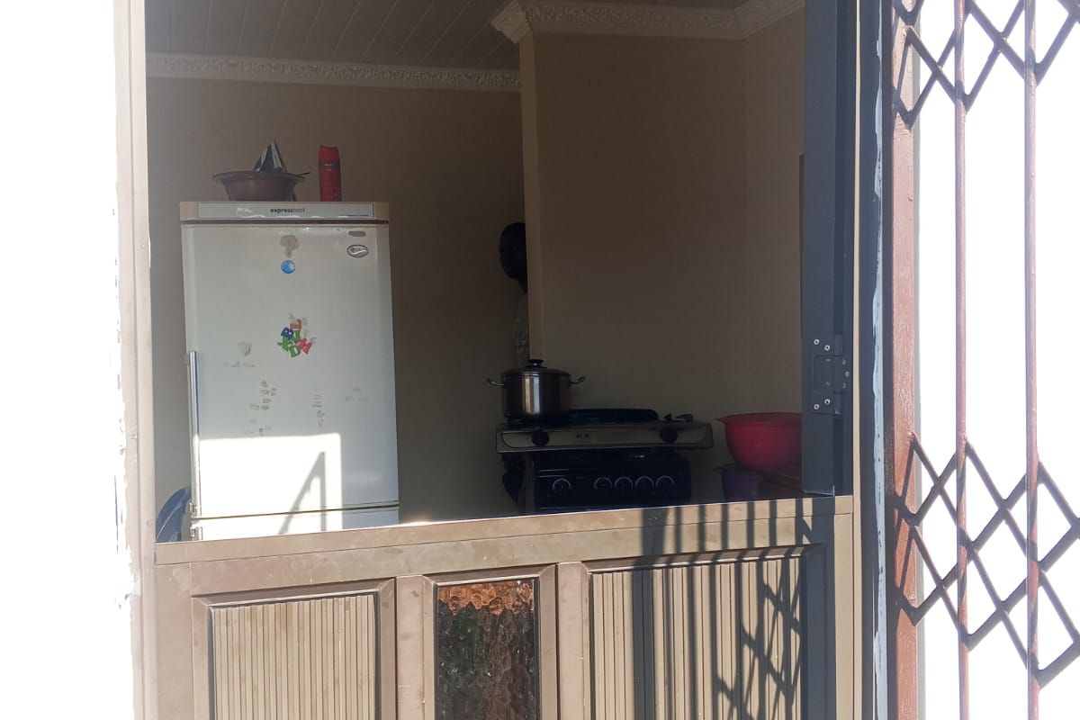 A view into a compact kitchen featuring a stable door entrance, security gate, and built-in stove, showing signs of age and wear.