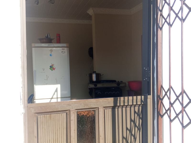 A view into a compact kitchen featuring a stable door entrance, security gate, and built-in stove, showing signs of age and wear.