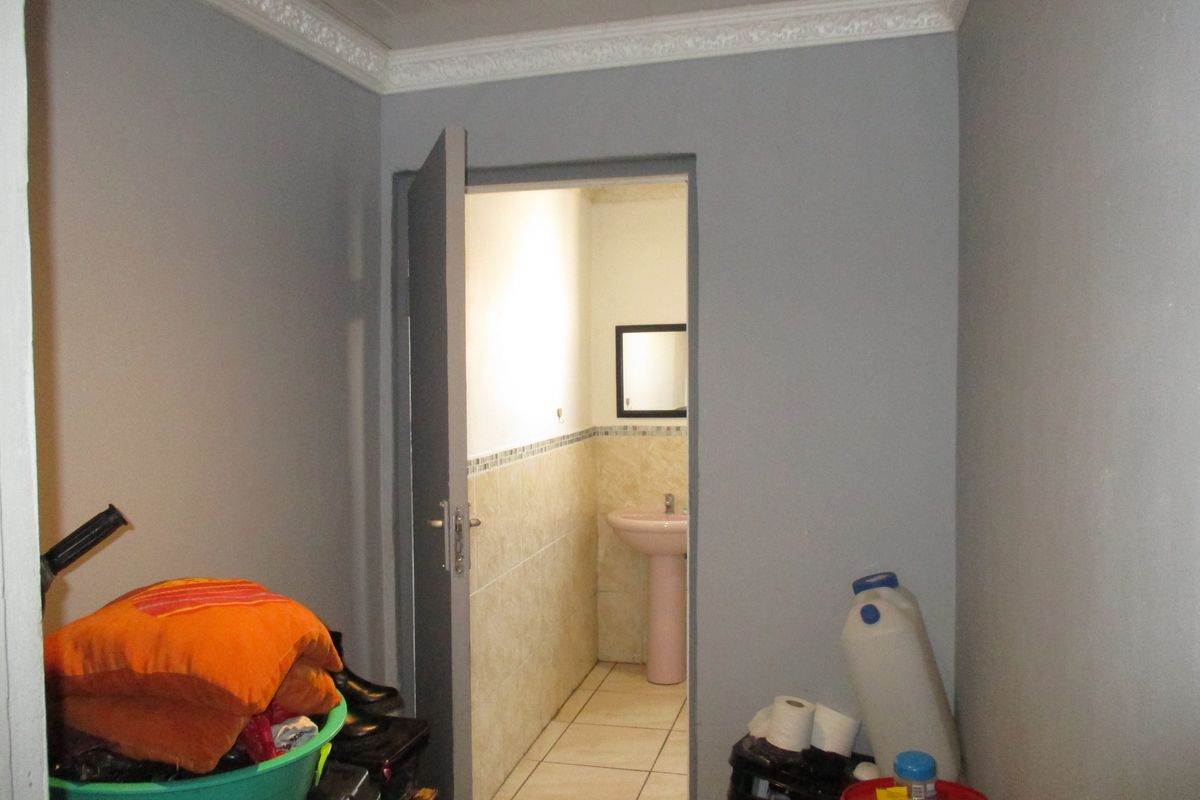A small bathroom featuring a pedestal basin, tiled flooring, and partial wall tiling, viewed from an adjacent storage or utility area.