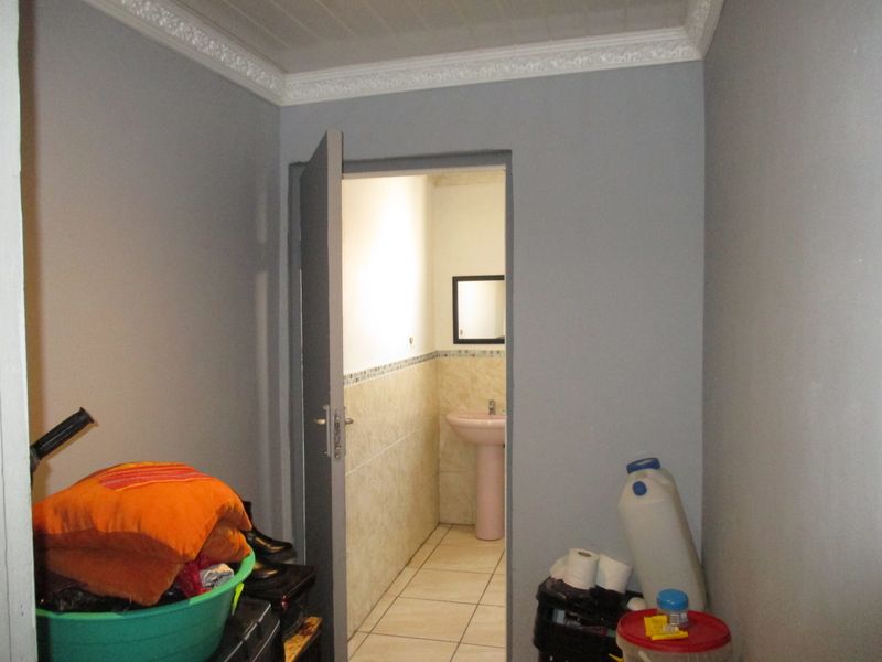 A small bathroom featuring a pedestal basin, tiled flooring, and partial wall tiling, viewed from an adjacent storage or utility area.