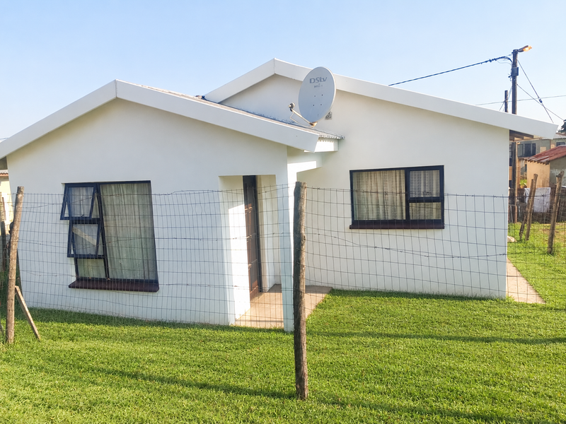 A well-maintained single-story residential house featuring a clean white facade, metal-framed windows, and a secure wire mesh perimeter fence.
