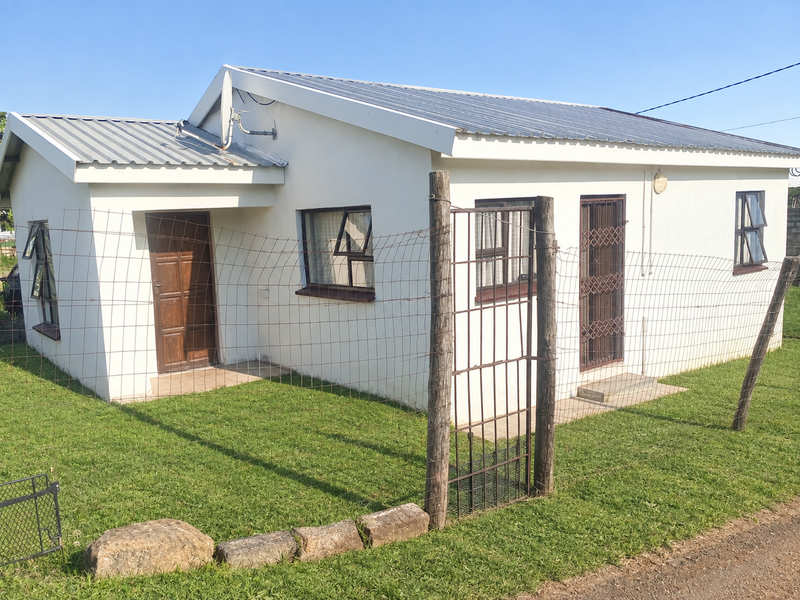 A single-story residential house featuring a corrugated metal roof, security gates, and top-hung windows, set within a fenced garden area.