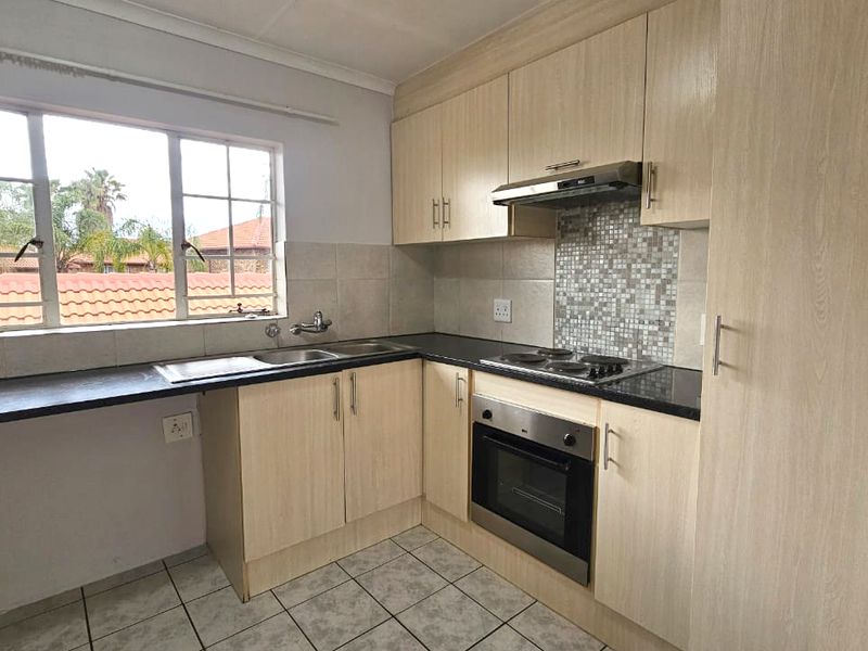 A functional kitchen featuring light wood-look cabinetry, a built-in oven with hob, mosaic backsplash, and tiled flooring with ample natural light.