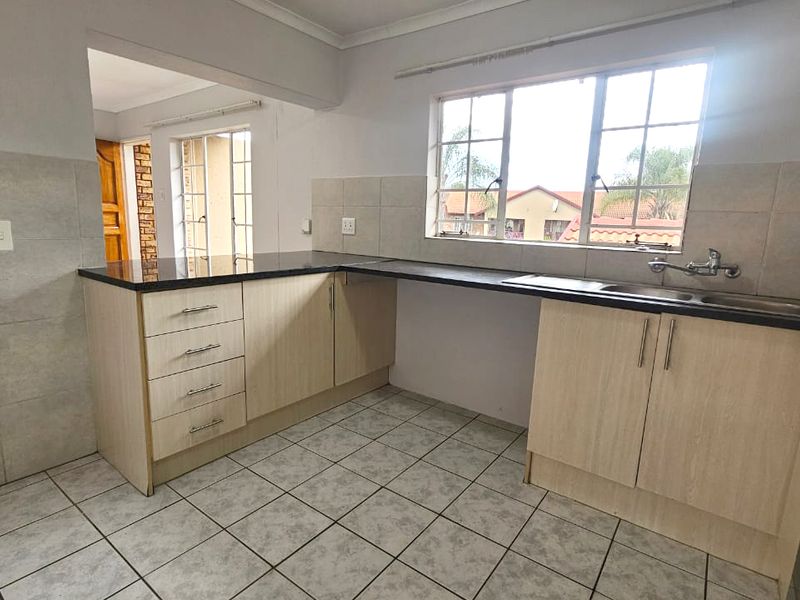 A functional kitchen featuring light wood-finish cabinetry, dark granite countertops, a double basin sink, and tiled flooring, offering a clean canvas for updates.