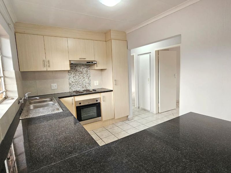 A functional kitchen featuring light wood cabinetry, dark granite countertops, built-in oven and hob, and tiled flooring, offering a clean and practical workspace.