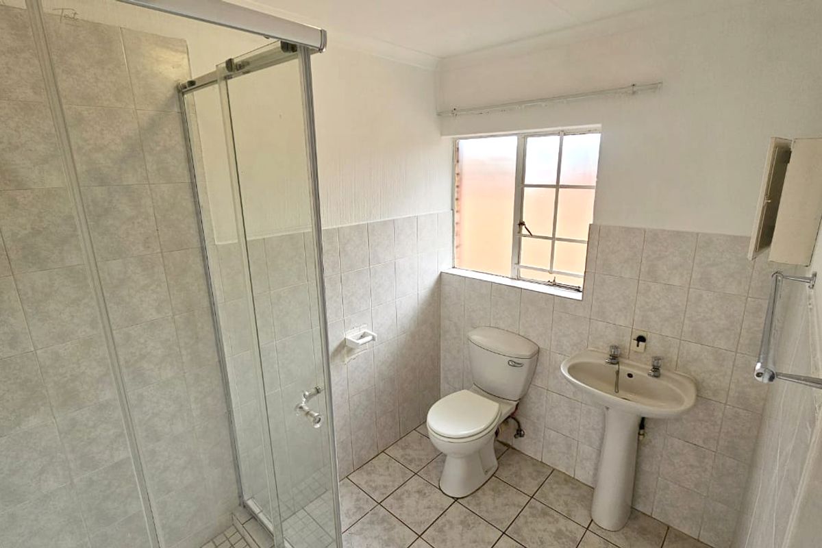 A functional bathroom featuring a glass shower enclosure, pedestal basin, and toilet with neutral wall and floor tiling.