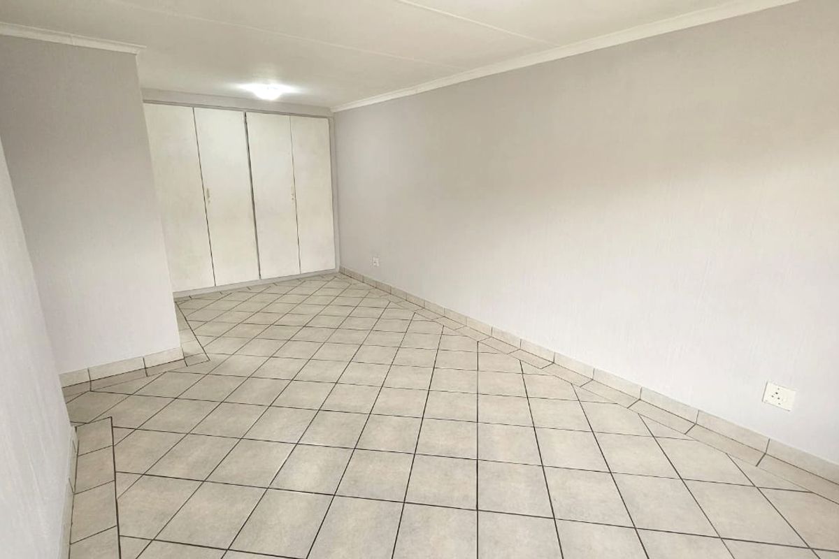 A spacious, empty bedroom featuring neutral tiled flooring, white walls, and built-in cupboards, providing a clean canvas for personalization.