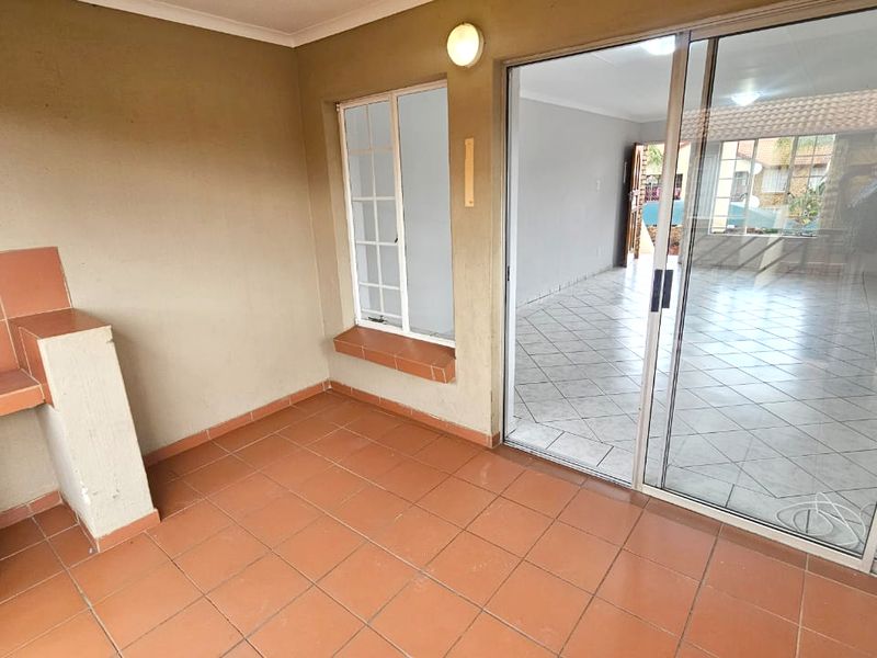 Covered patio area featuring a built-in braai, tiled flooring, and sliding glass doors providing access to the interior living space.