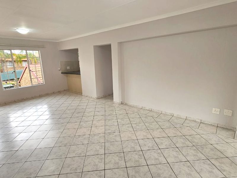 Spacious open-plan living area featuring neutral tiled flooring, coved ceilings, and a functional kitchen nook, offering a bright and versatile layout.