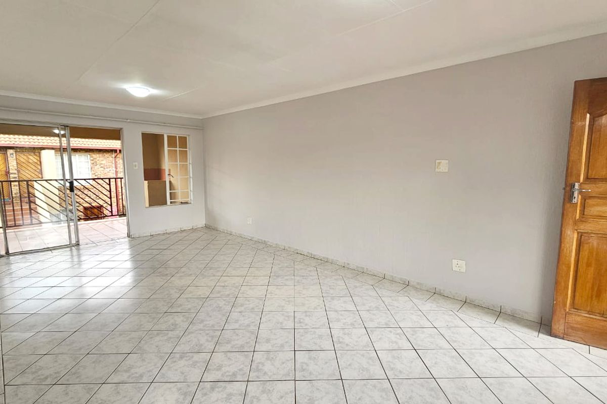 Spacious, light-filled living area featuring neutral tiled flooring, a coved ceiling, and direct access to an outdoor patio through sliding glass doors.