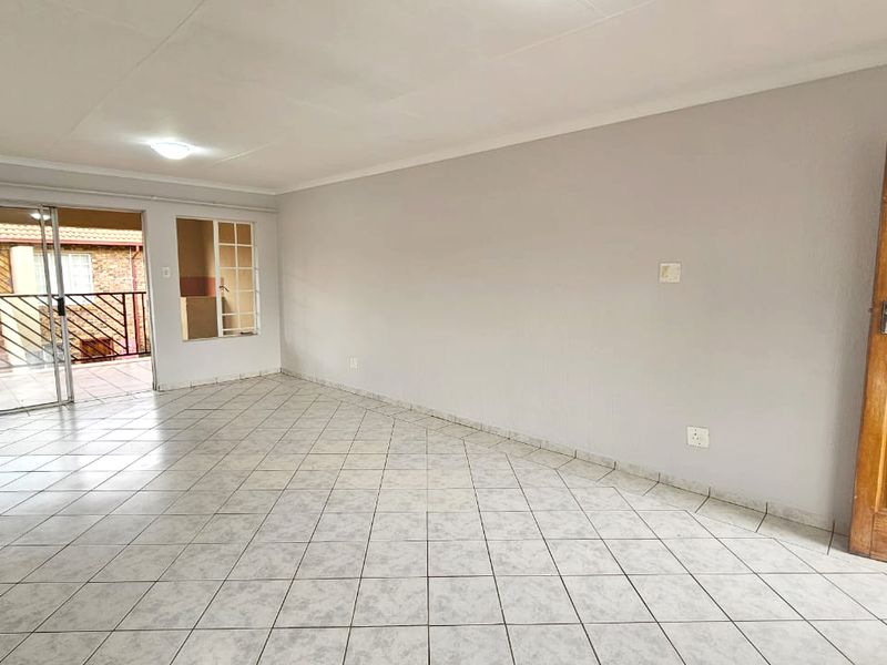 Spacious, light-filled living area featuring neutral tiled flooring, a coved ceiling, and direct access to an outdoor patio through sliding glass doors.