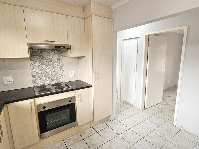 A clean, functional kitchen featuring light wood-finish cabinetry, dark countertops, a built-in oven and hob, and neutral tiled flooring.
