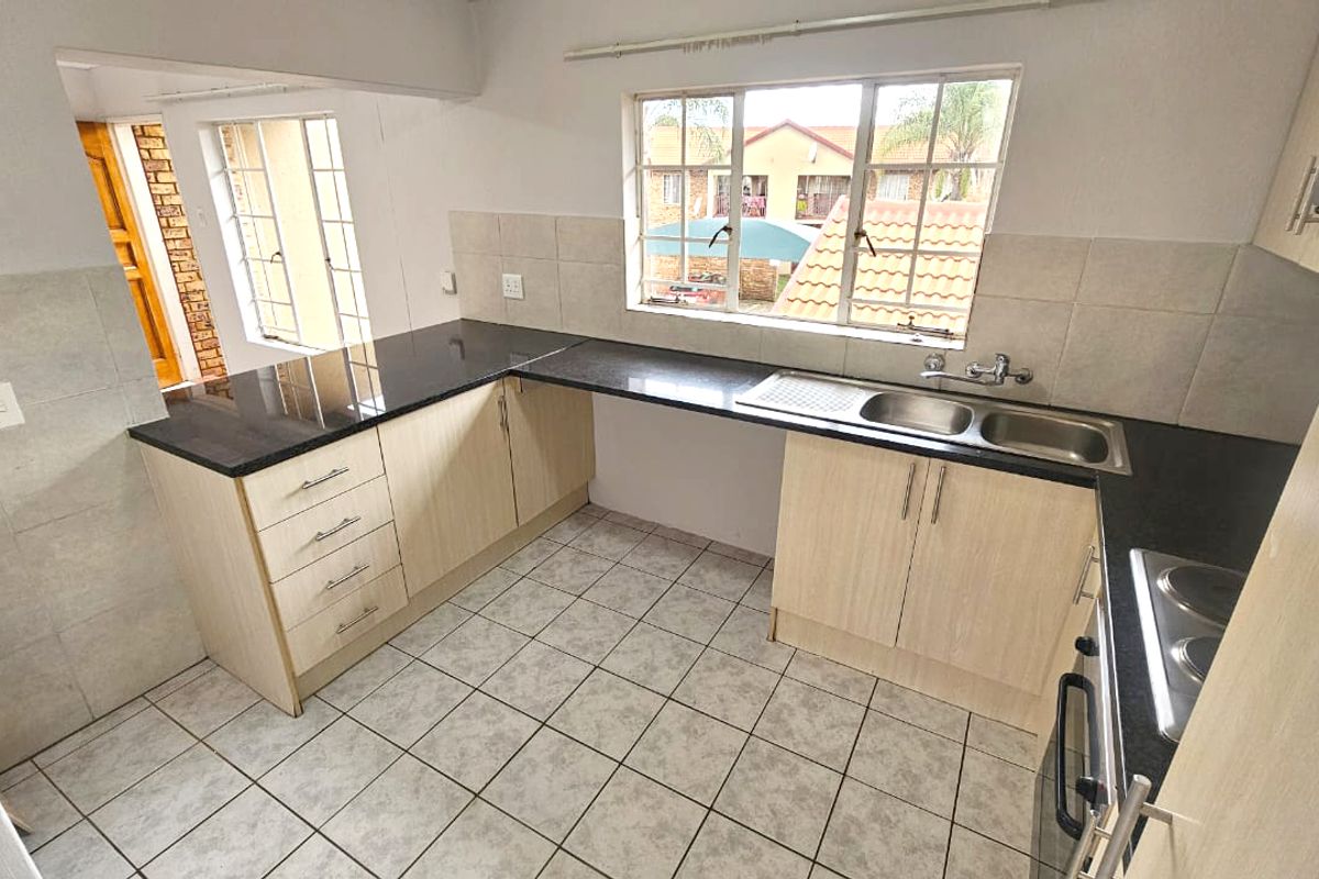 A functional kitchen featuring granite countertops, light wood-finish cabinetry, a double stainless steel sink, and tiled flooring with ample natural light.