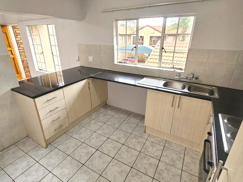 A functional kitchen featuring granite countertops, light wood-finish cabinetry, a double stainless steel sink, and tiled flooring with ample natural light.
