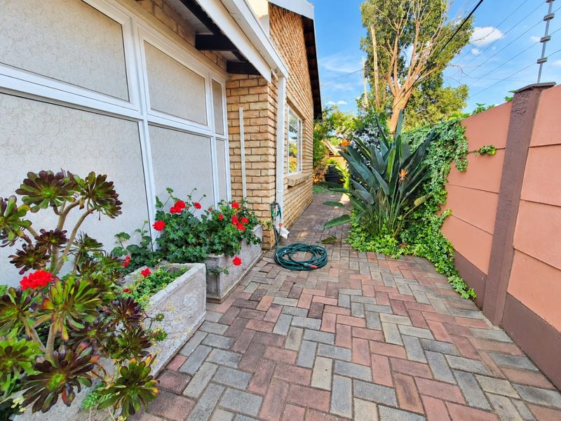 A side walkway featuring brick paving, face brick exterior wall, and a secure boundary wall with electric fencing.