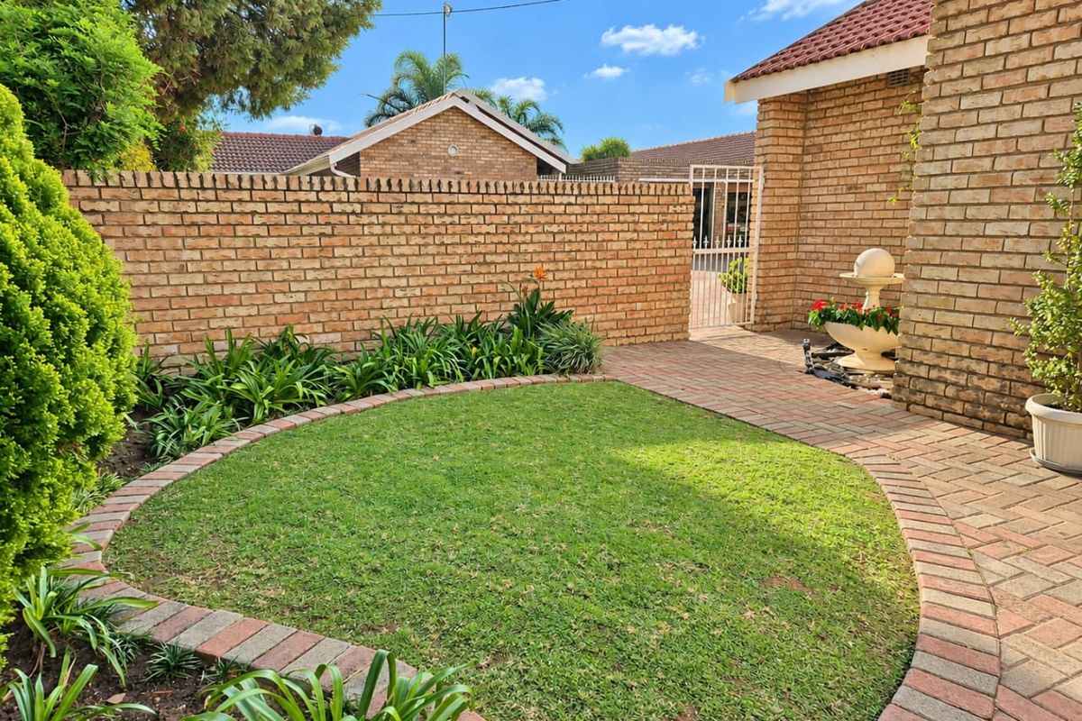 A well-maintained rear garden area featuring a circular lawn, brick paving, and a secure gated entrance.
