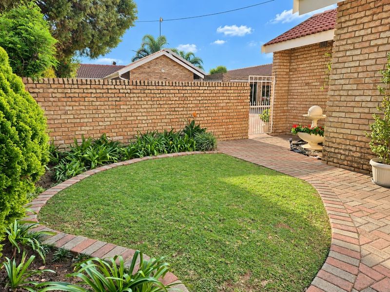 A well-maintained rear garden area featuring a circular lawn, brick paving, and a secure gated entrance.