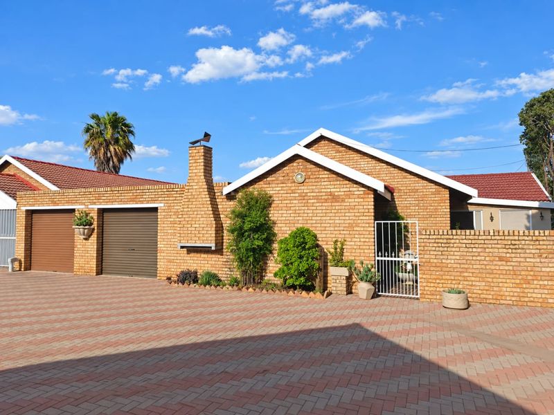 Front elevation of a face brick townhouse featuring a double garage, paved driveway, and a built-in outdoor braai area.