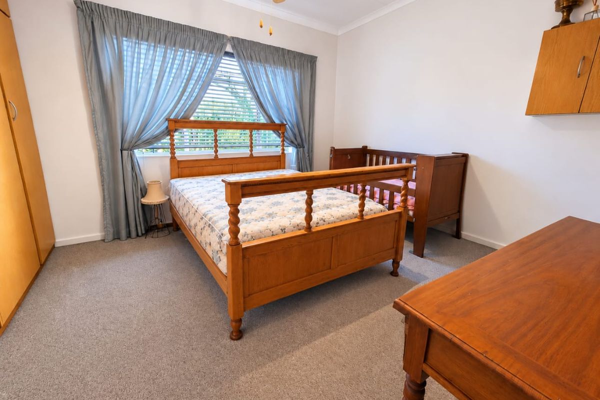 A spacious bedroom featuring neutral walls, carpeted flooring, a ceiling fan, and a built-in wardrobe, offering a functional and comfortable living space.