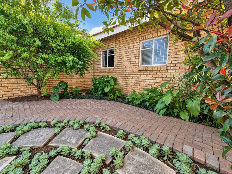 A well-maintained rear exterior view featuring a brick facade, paved walkway, and landscaped garden area with stone pavers.
