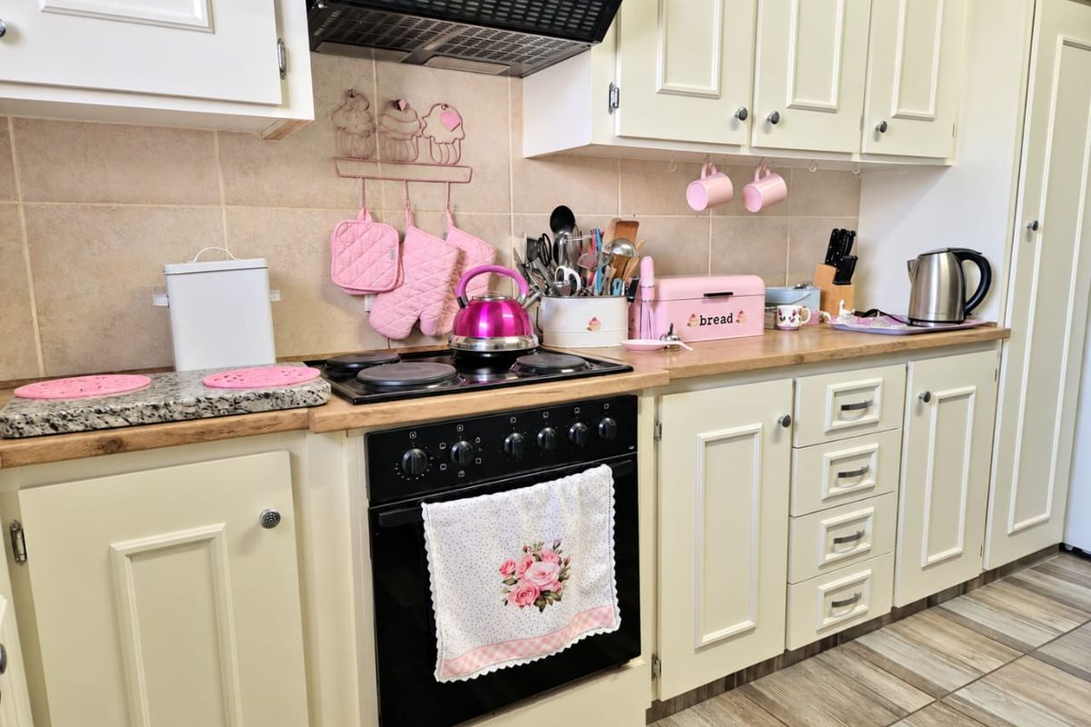 A functional kitchen featuring cream-colored cabinetry, a built-in oven with electric hob, extractor fan, and tiled backsplash with wood-look laminate countertops.