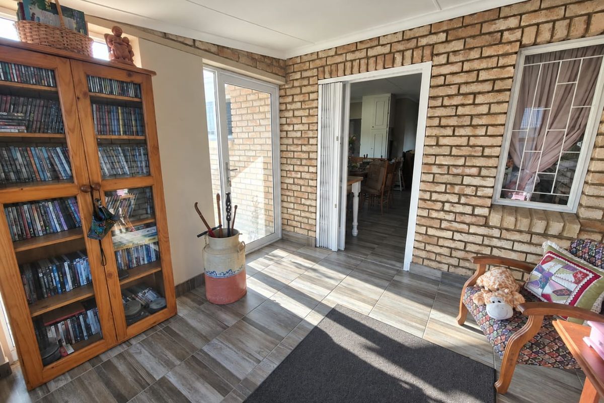 A sunlit living area featuring exposed brick walls, tiled flooring, and access to adjacent rooms through a folding door and glass sliding door.