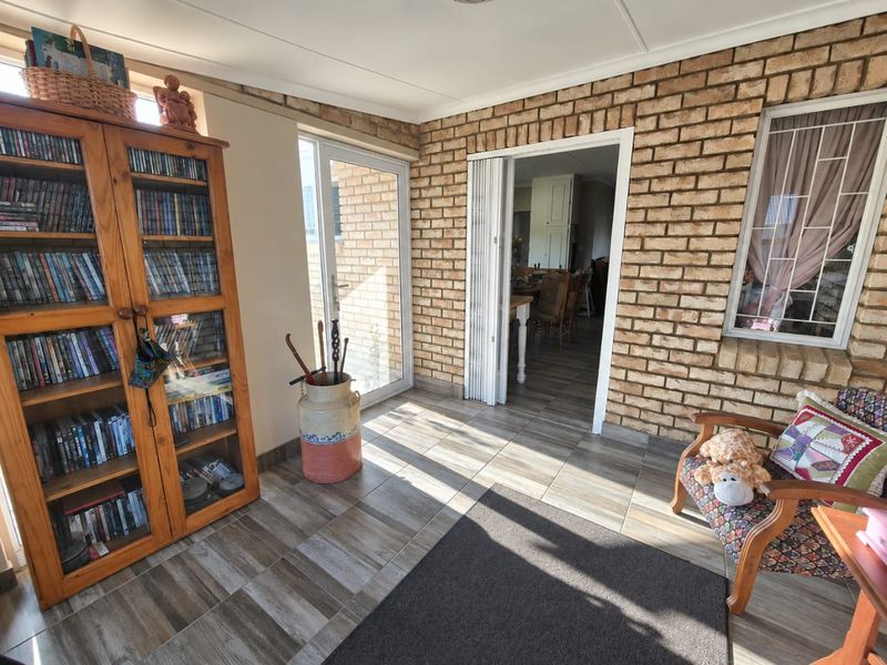 A sunlit living area featuring exposed brick walls, tiled flooring, and access to adjacent rooms through a folding door and glass sliding door.