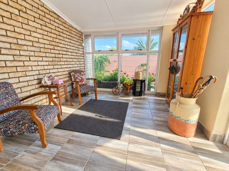 A bright, enclosed patio featuring exposed brickwork, wood-look tiled flooring, and large windows providing natural light and garden views.