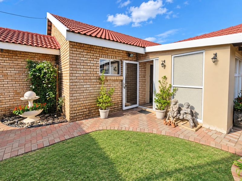 A well-maintained rear exterior view of a townhouse featuring a brick facade, tiled roof, paved walkway, and a manicured lawn.