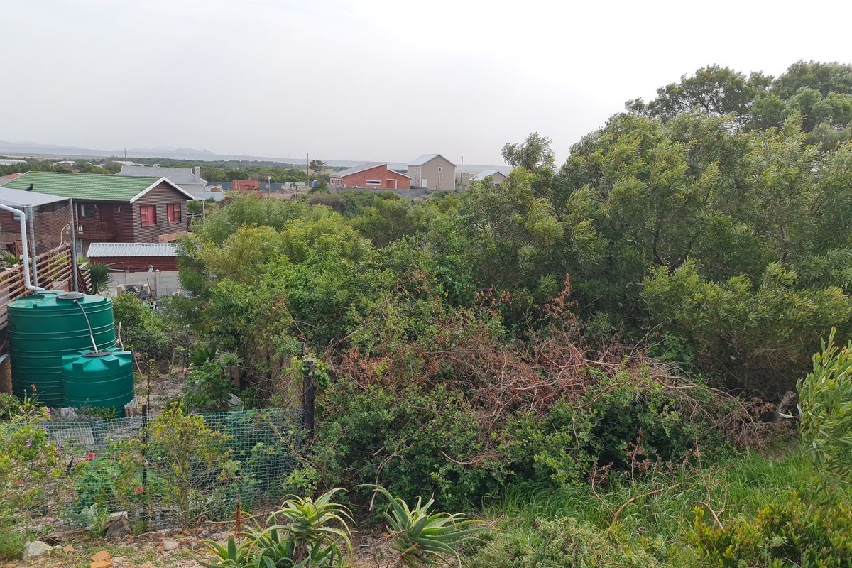 A view of a residential plot featuring dense native vegetation, wire mesh fencing, and installed water storage tanks.