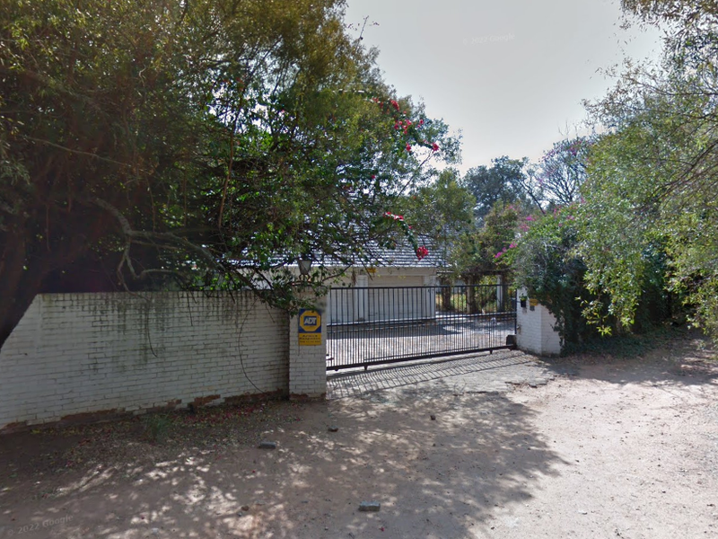 Front entrance view of the property featuring a sliding security gate, perimeter wall, and mature trees providing privacy.