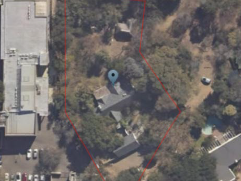An aerial view of a residential vacant land plot featuring mature trees and defined property boundaries.