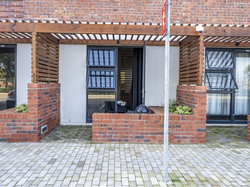 Front exterior view of an apartment featuring a brick facade, timber pergola, paved entrance area, and integrated brick planter boxes.