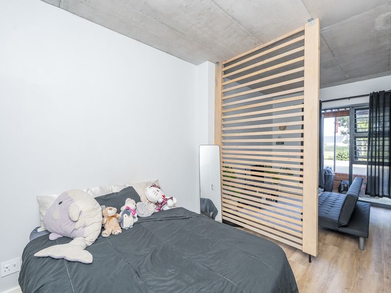 Modern bedroom featuring an exposed concrete ceiling, timber slat room divider, and direct access to an outdoor area through a sliding glass door.