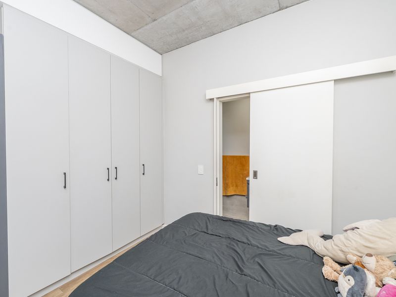 Modern bedroom featuring built-in cupboards, exposed concrete ceiling, and a sliding door leading to an en-suite bathroom.