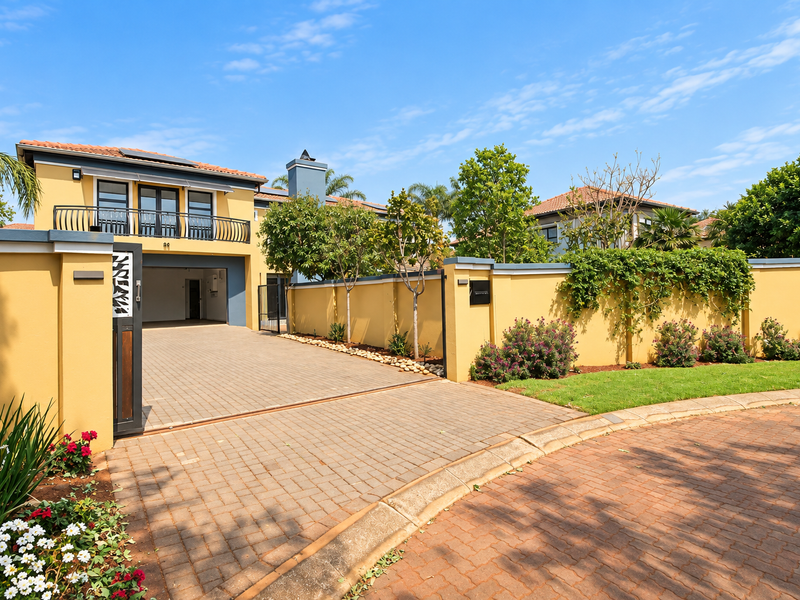 A well-maintained residential property featuring a paved driveway, secure boundary wall, and a balcony overlooking the front entrance.