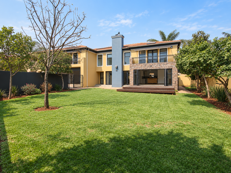 Spacious rear garden featuring a well-maintained lawn, timber decking, and a two-story home facade with stone accents and bi-fold doors.