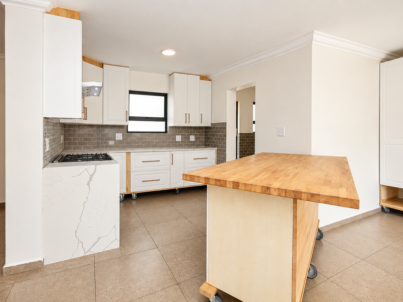 Modern kitchen featuring white cabinetry, stone countertops, a gas hob, tiled backsplash, and a mobile wooden kitchen island on casters.