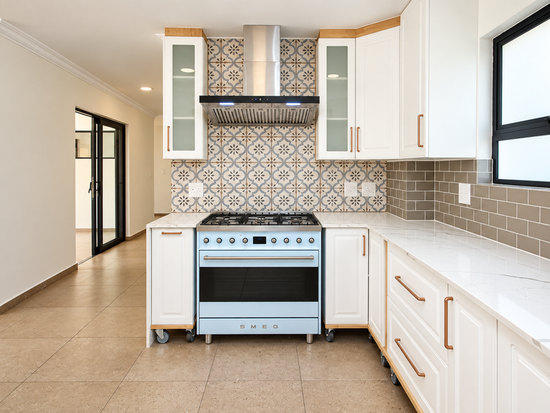 Modern kitchen featuring a signature blue Smeg gas stove, patterned tile backsplash, white shaker cabinetry, and quartz countertops with a clean, contemporary finish.