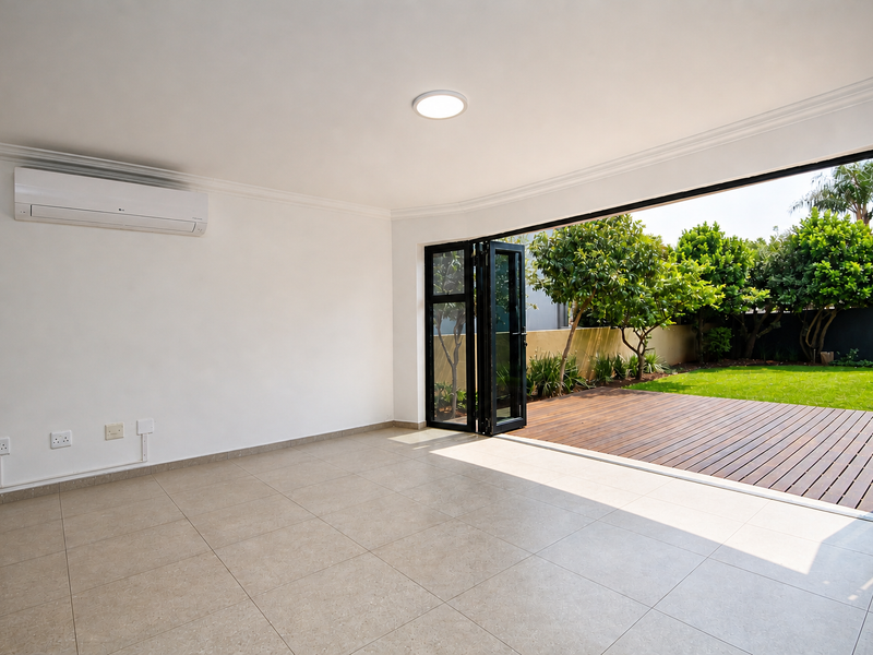Bright, open-plan living area featuring large bi-fold doors that open onto a wooden deck and garden, complete with a wall-mounted air conditioning unit.