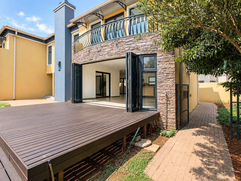 Rear view of the property featuring a large timber deck, stone-clad facade, bi-fold doors leading to the interior, and a paved garden walkway.
