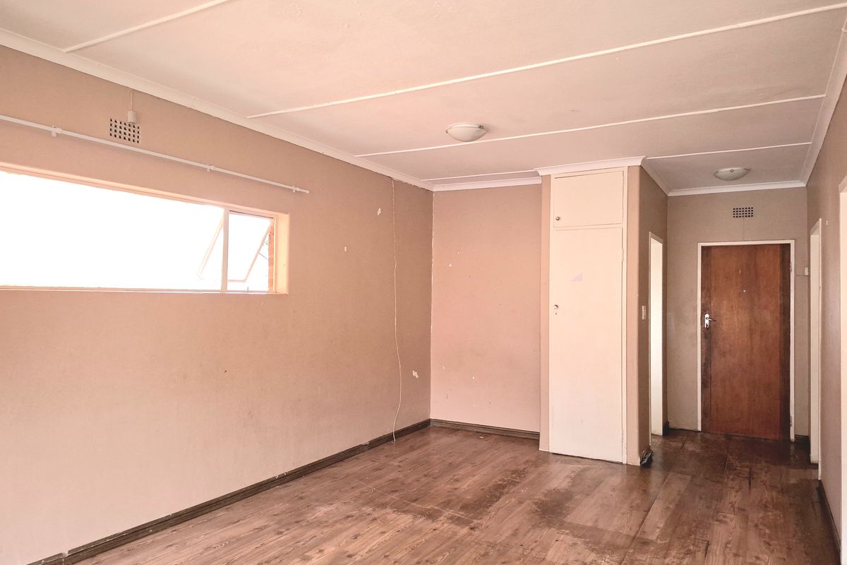 An empty living room featuring laminate flooring, a built-in cupboard, and neutral wall tones, offering a blank canvas for renovation or interior design.