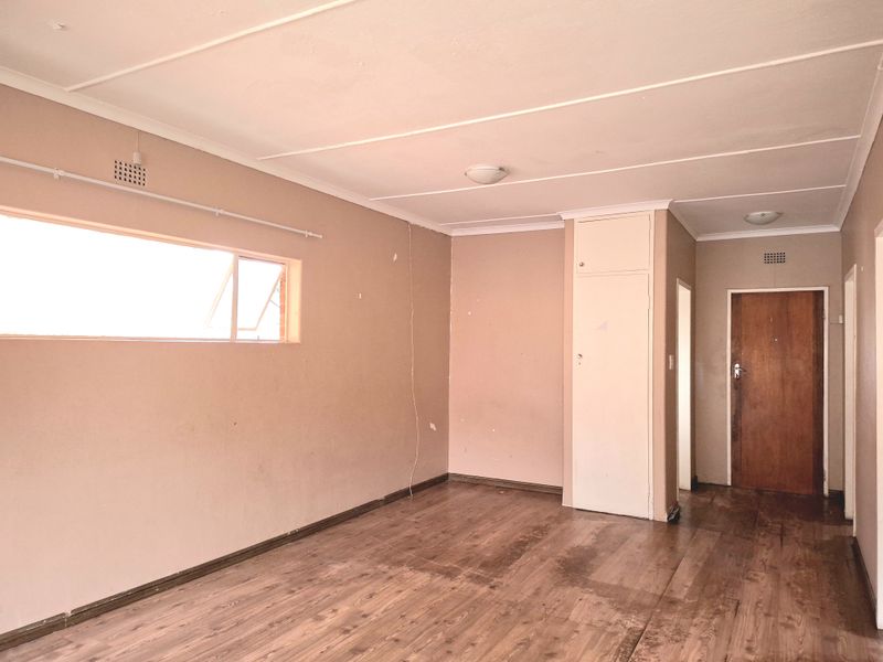 An empty living room featuring laminate flooring, a built-in cupboard, and neutral wall tones, offering a blank canvas for renovation or interior design.