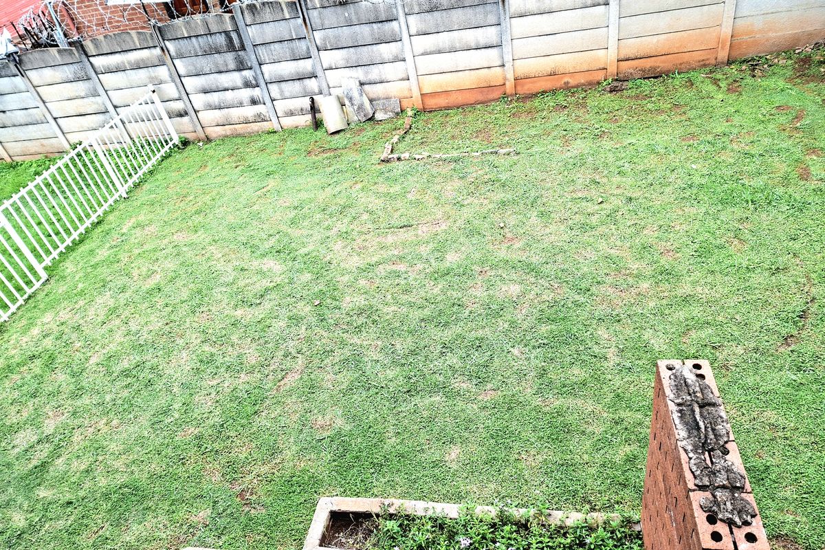 A private rear garden area featuring a lawn, a brick planter box, and a secure perimeter boundary wall with razor wire.